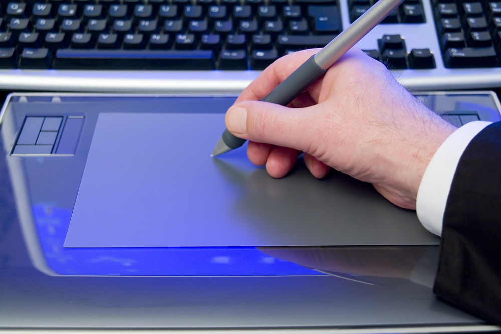 Dłoń z ryskiem pracująca na tablecie graficznym leżącym obok komputera